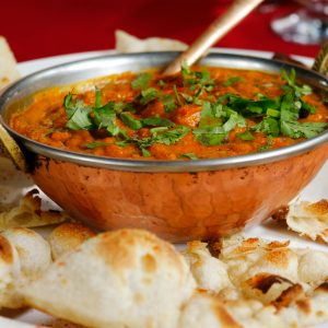 Delicious Indian curry garnished with cilantro served with naan in a copper dish.